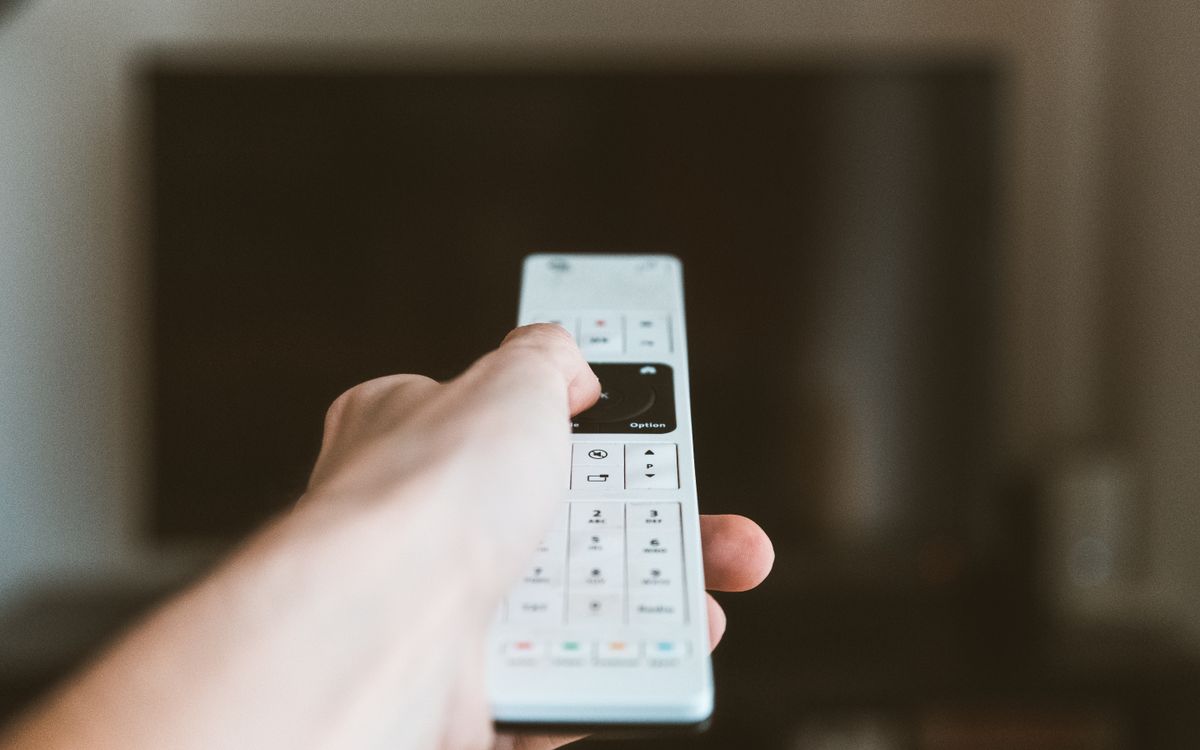 A hand using a television remote indoors